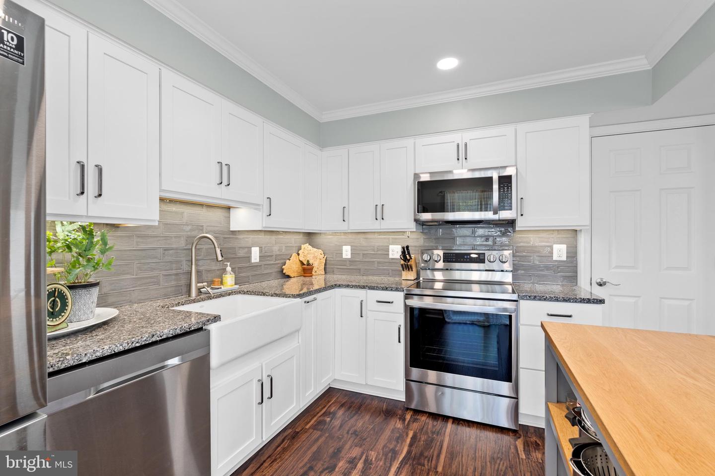 Kitchen with white cabinets, gray tile backsplash, granite counters, and stainless steel appliances.