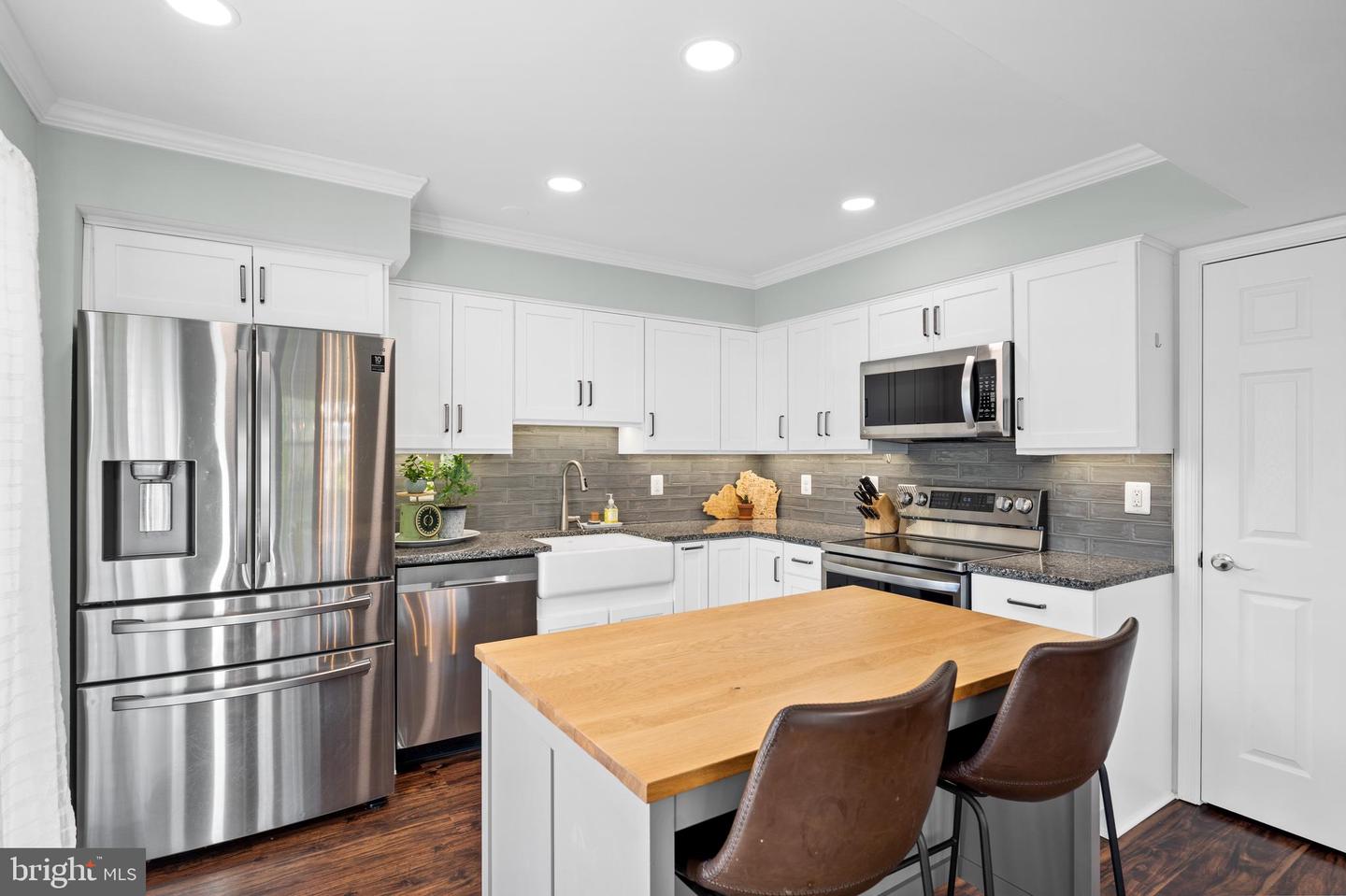 Kitchen with white cabinets, stainless steel appliances, gray tile backsplash, and a large wood-top island.
