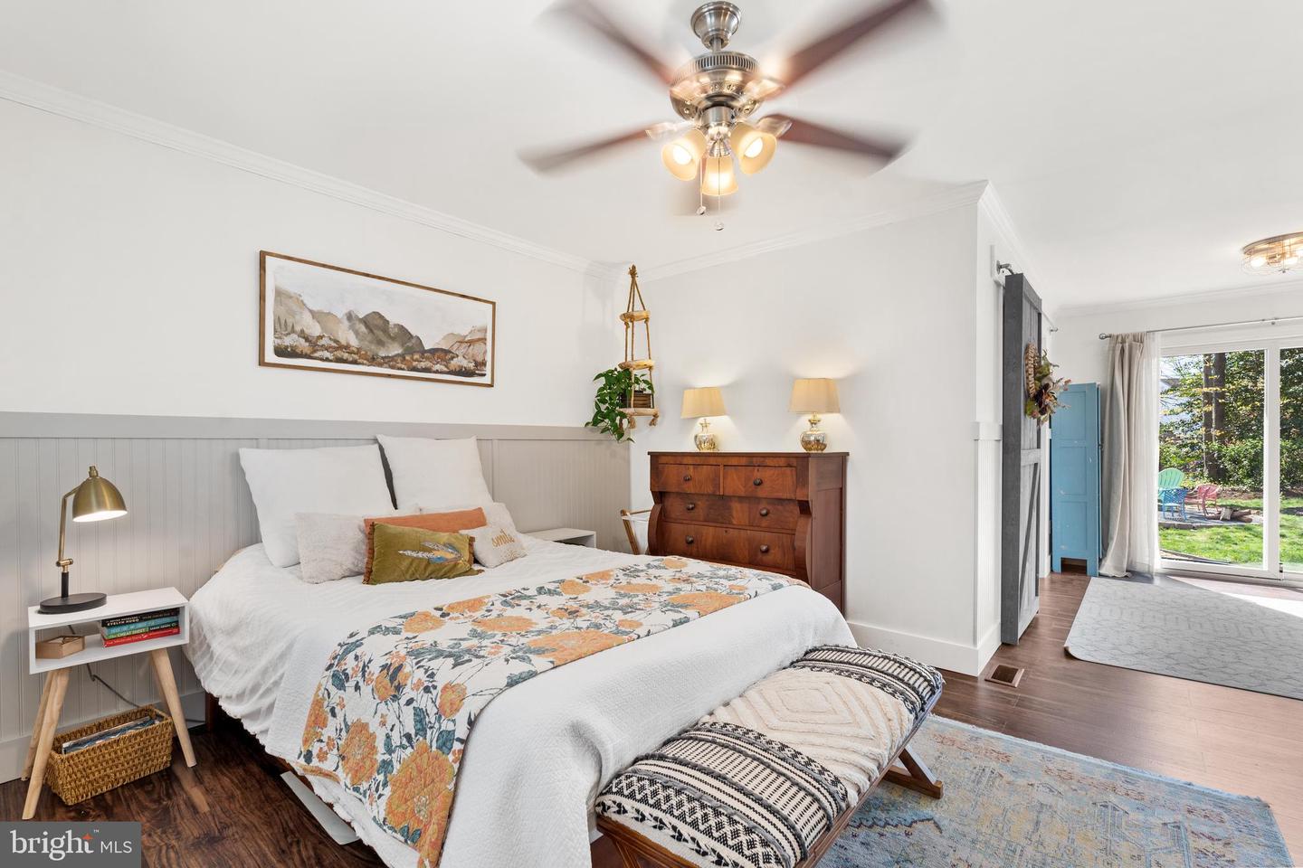 Bedroom with a white bed, floral runner, gray paneled walls, and sliding doors to a garden patio.