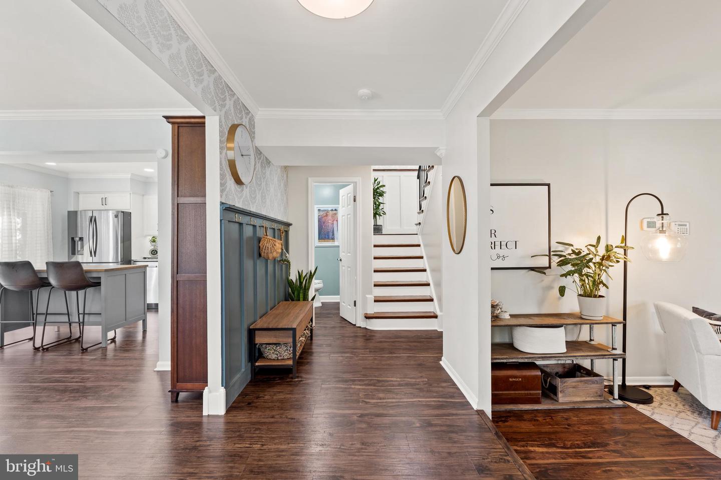 Entry hall with dark wood floors, blue paneled wall, staircase, and views into the kitchen and sitting area.
