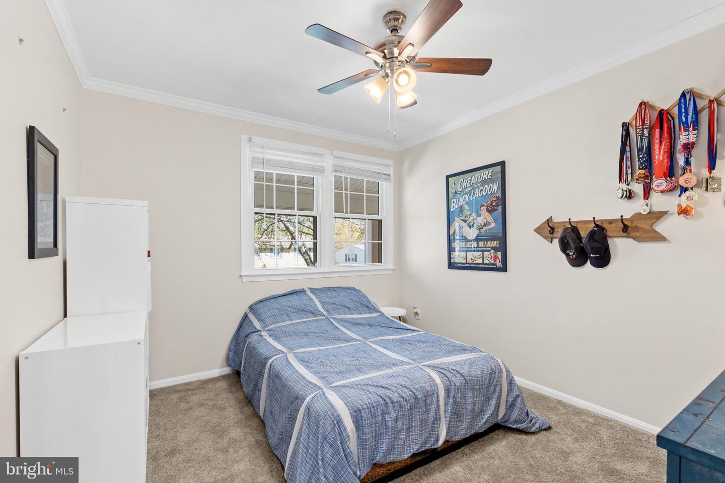 Bedroom with a blue plaid-covered bed, two windows, and medals displayed on the wall.