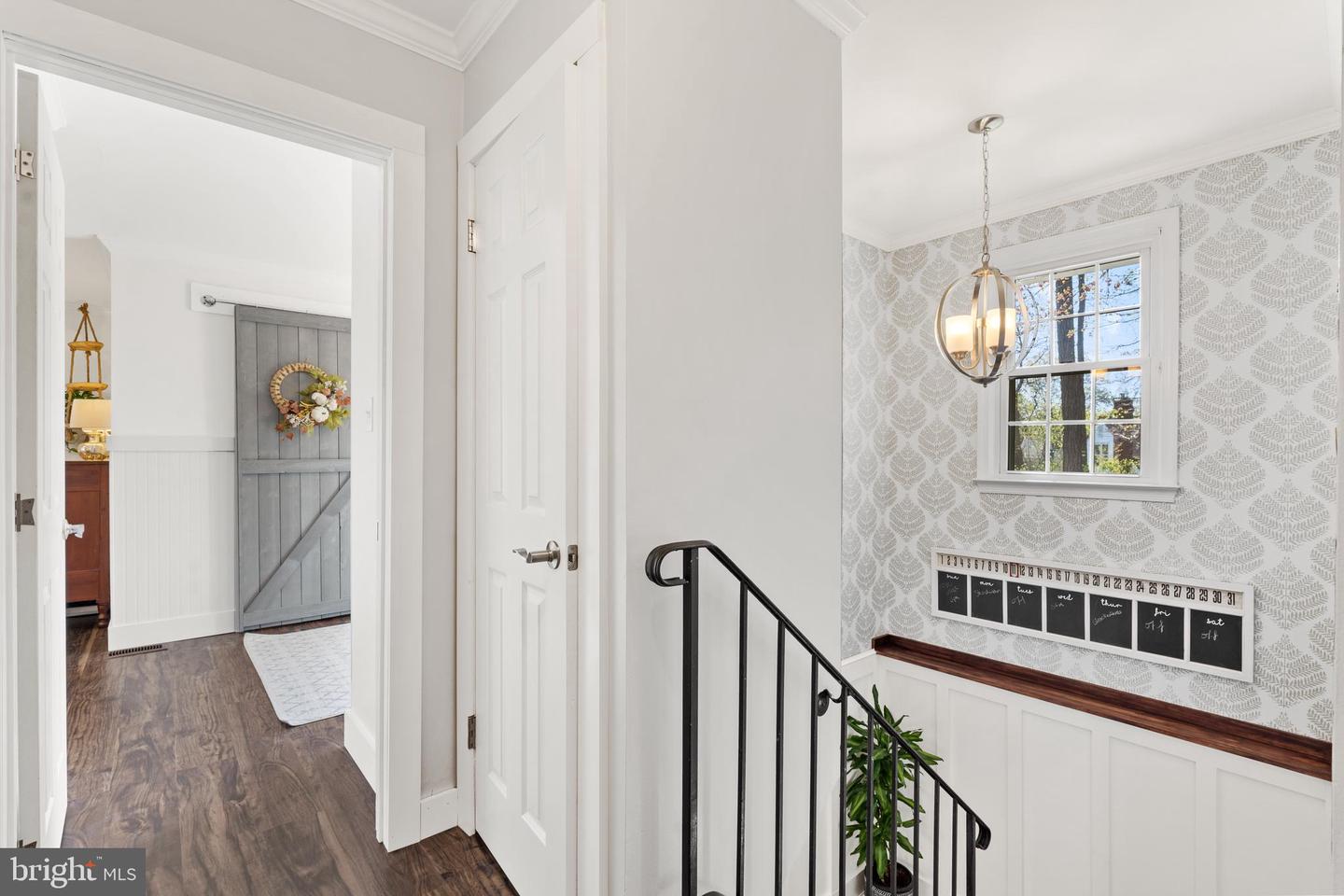 Upstairs landing with patterned wallpaper, white wainscoting, and a black stair railing.