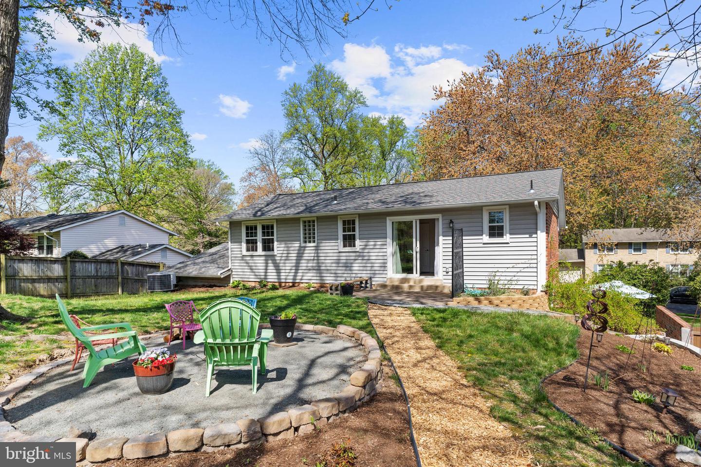 Rear exterior of a gray-sided home with a stone-edged patio and colorful outdoor chairs.