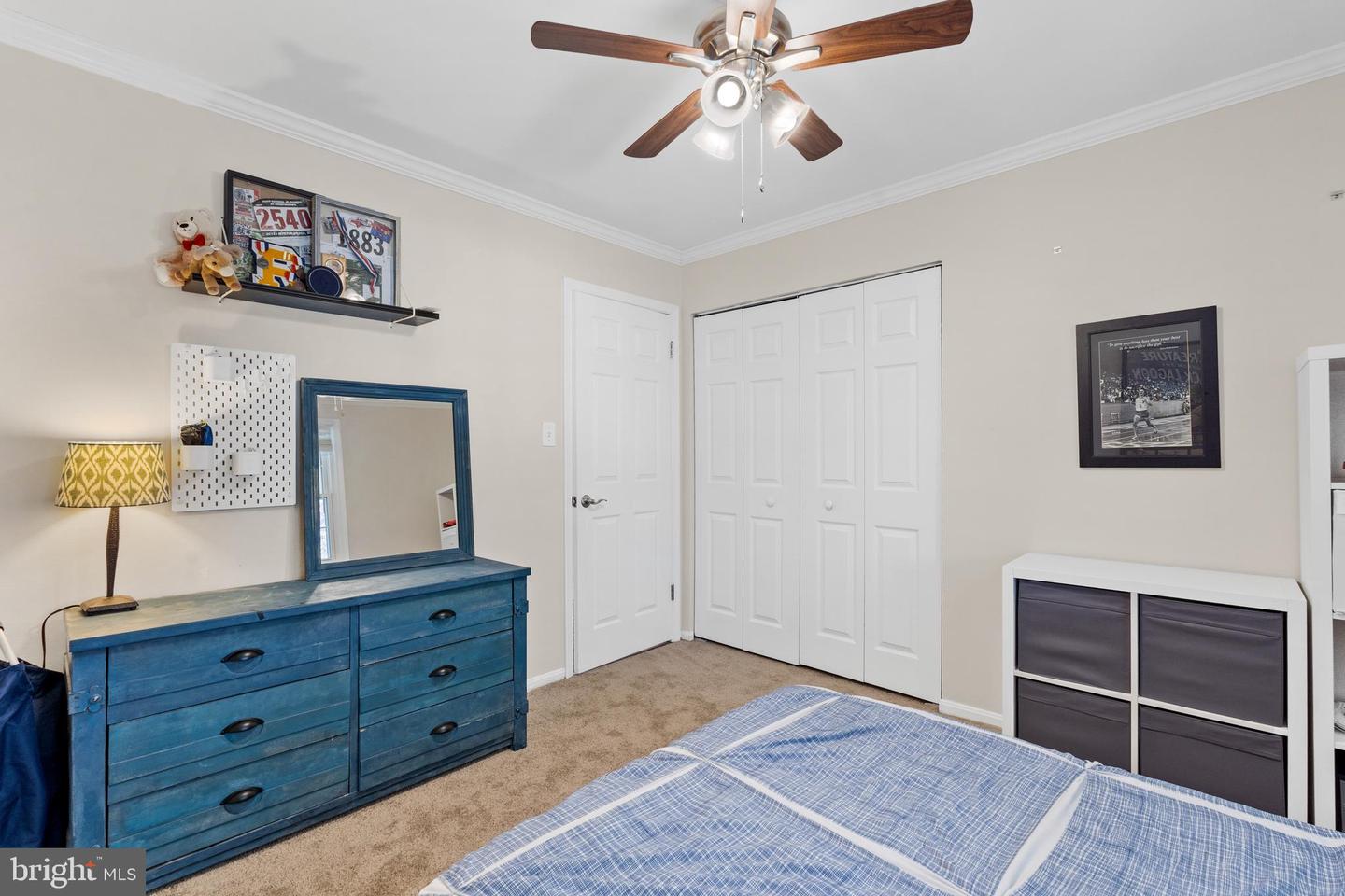Bedroom with a blue dresser and mirror, white closet doors, and a blue plaid bedspread.