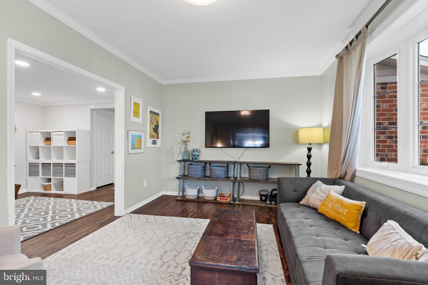 Living room with a gray sectional, wall-mounted television, and large windows beside a patterned rug.