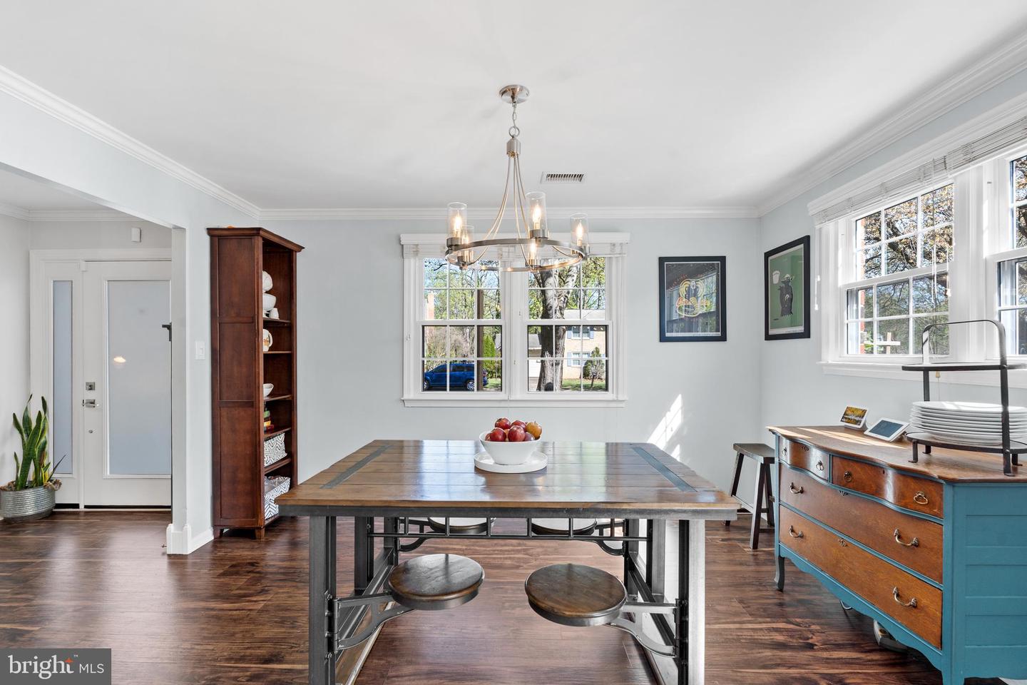 Dining room with a large wooden table, chandelier, tall windows, and blue sideboard.