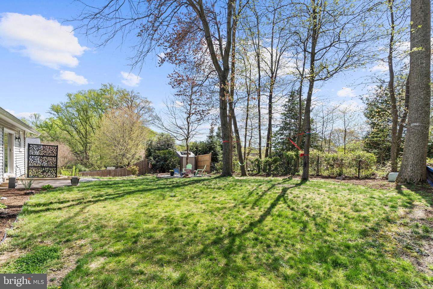 Backyard with a broad lawn, mature trees, and a small patio beside the house.
