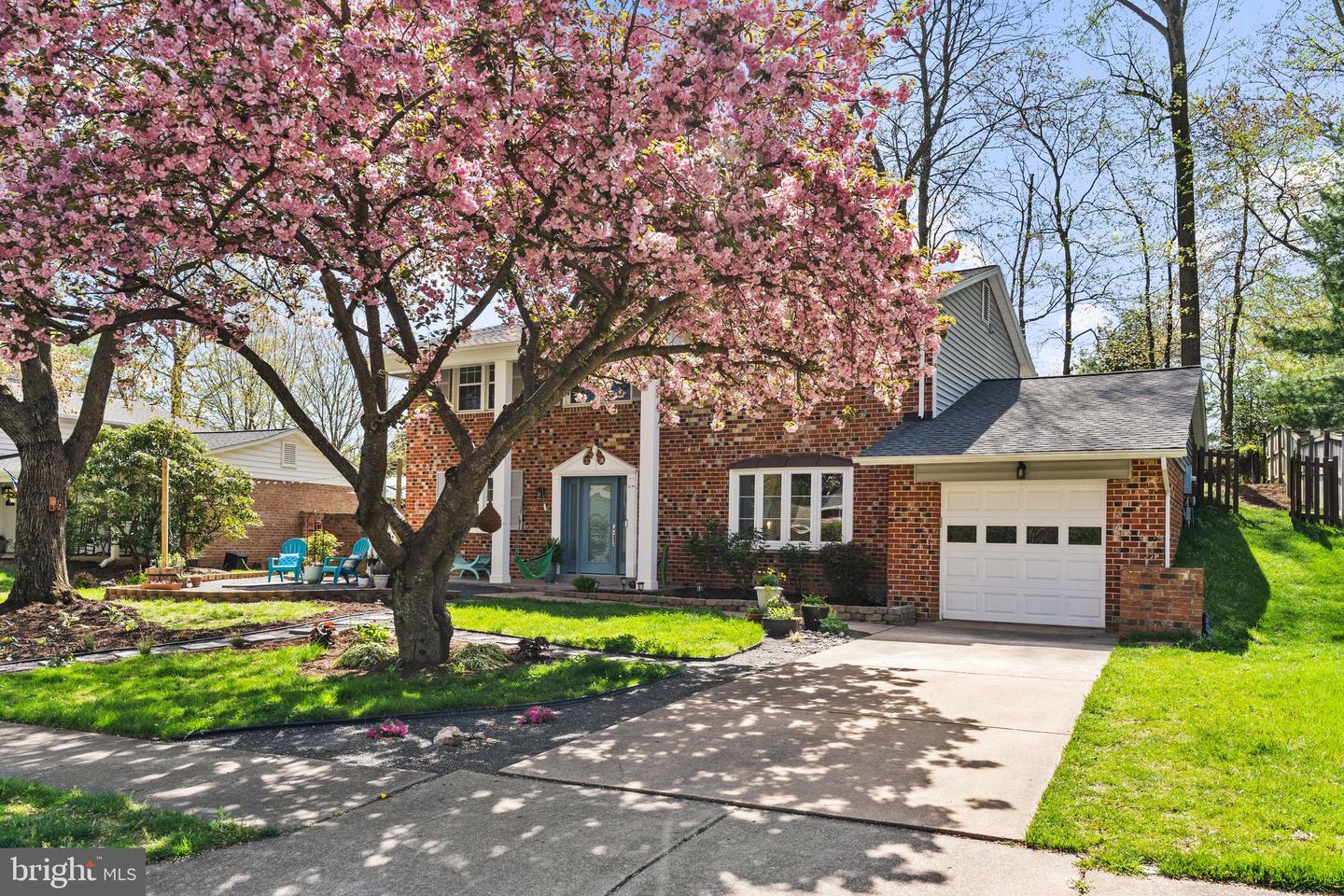 Two-story brick home framed by pink flowering trees, with an attached garage and patio.