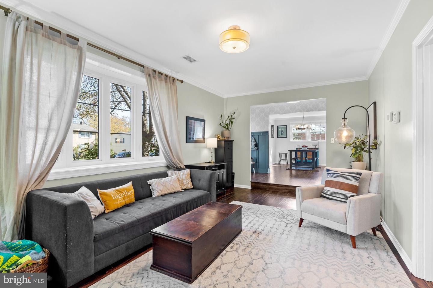 Staged living room with a charcoal sofa beneath large windows and an open doorway to the dining area.