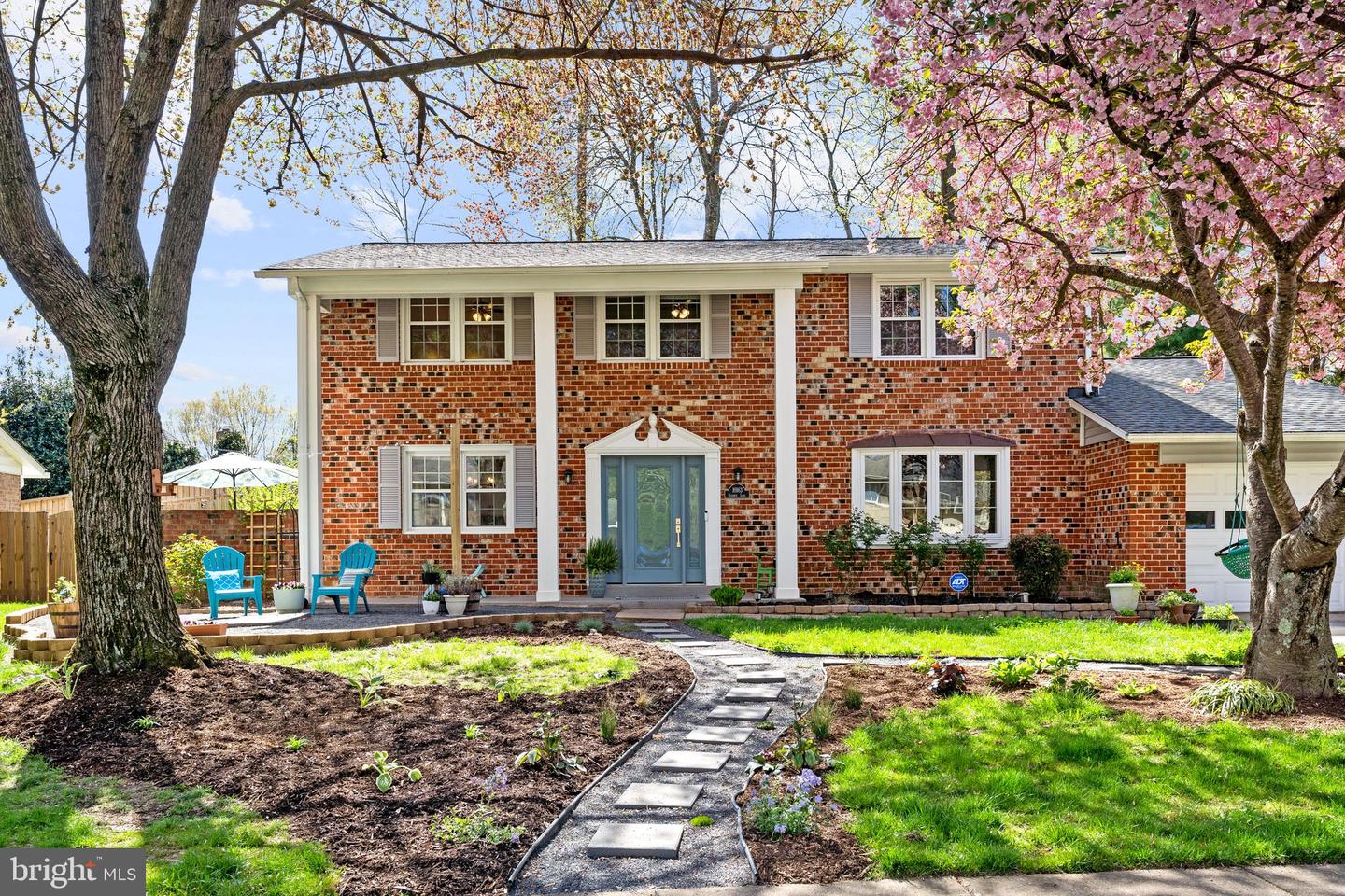 Two-story brick house with a blue front door, curved walkway, and flowering pink tree.