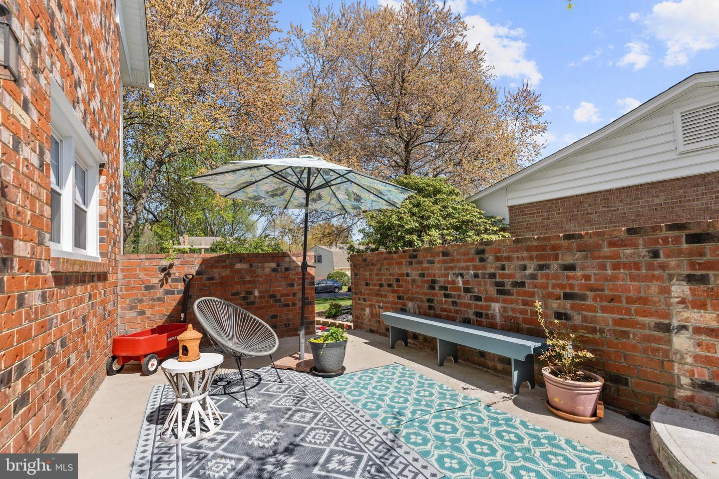 Brick patio with patterned rugs, an umbrella, outdoor seating, and potted plants.