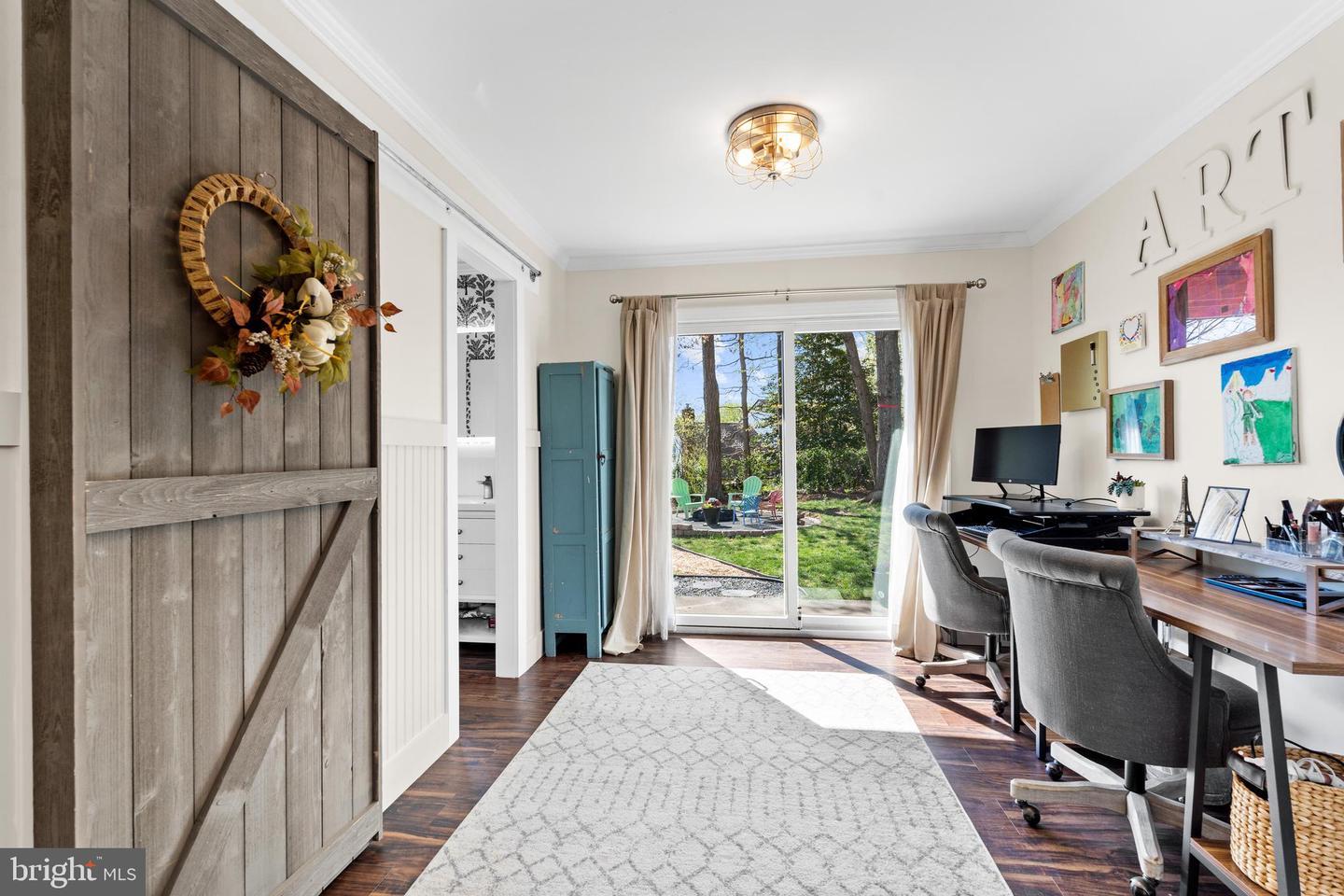 Home office with a sliding glass door overlooking a leafy backyard and a rustic barn-style door.