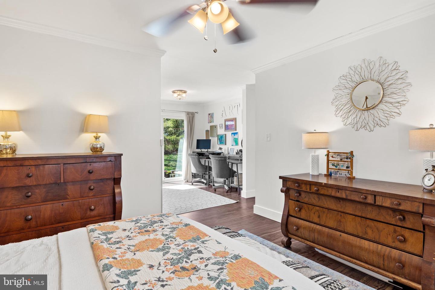 Furnished bedroom with dark wood dressers and a doorway opening to a bright home office.
