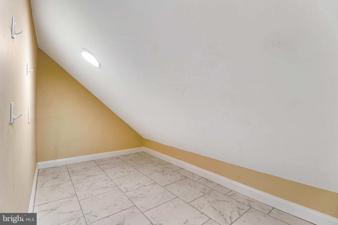 Empty room beneath a sloped ceiling with marble-pattern tile flooring and wall hooks.