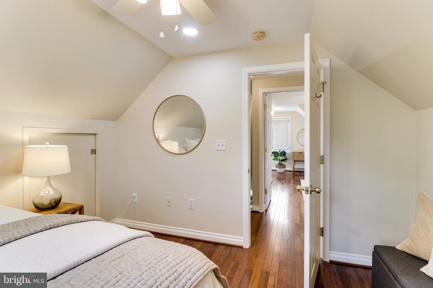 Bedroom with a sloped ceiling, hardwood floors, and an open doorway to a bright adjoining room.