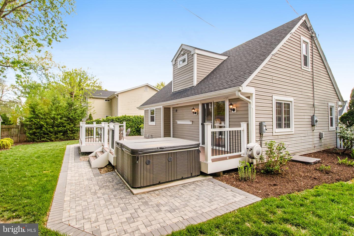 House rear exterior with a paved patio, hot tub, and raised deck.