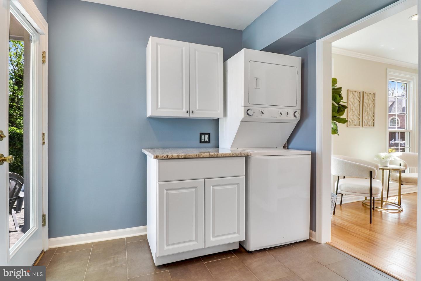 Laundry room with a white washer-dryer unit, cabinetry, and a countertop against blue walls.