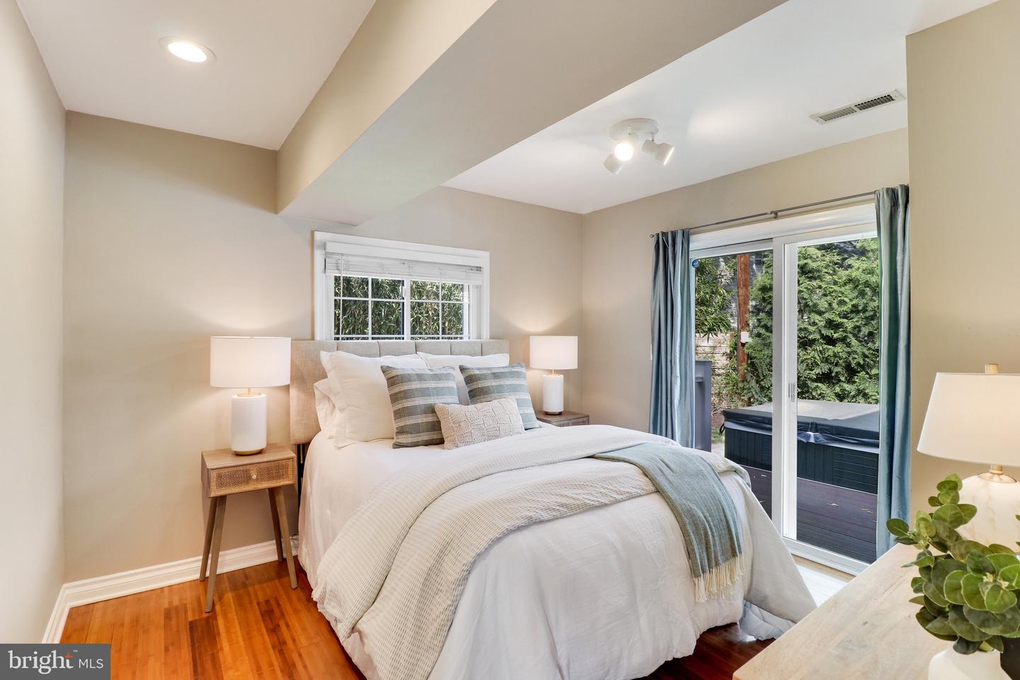 Staged bedroom with a white bed, warm wood floors, and sliding doors opening to a deck and hot tub.
