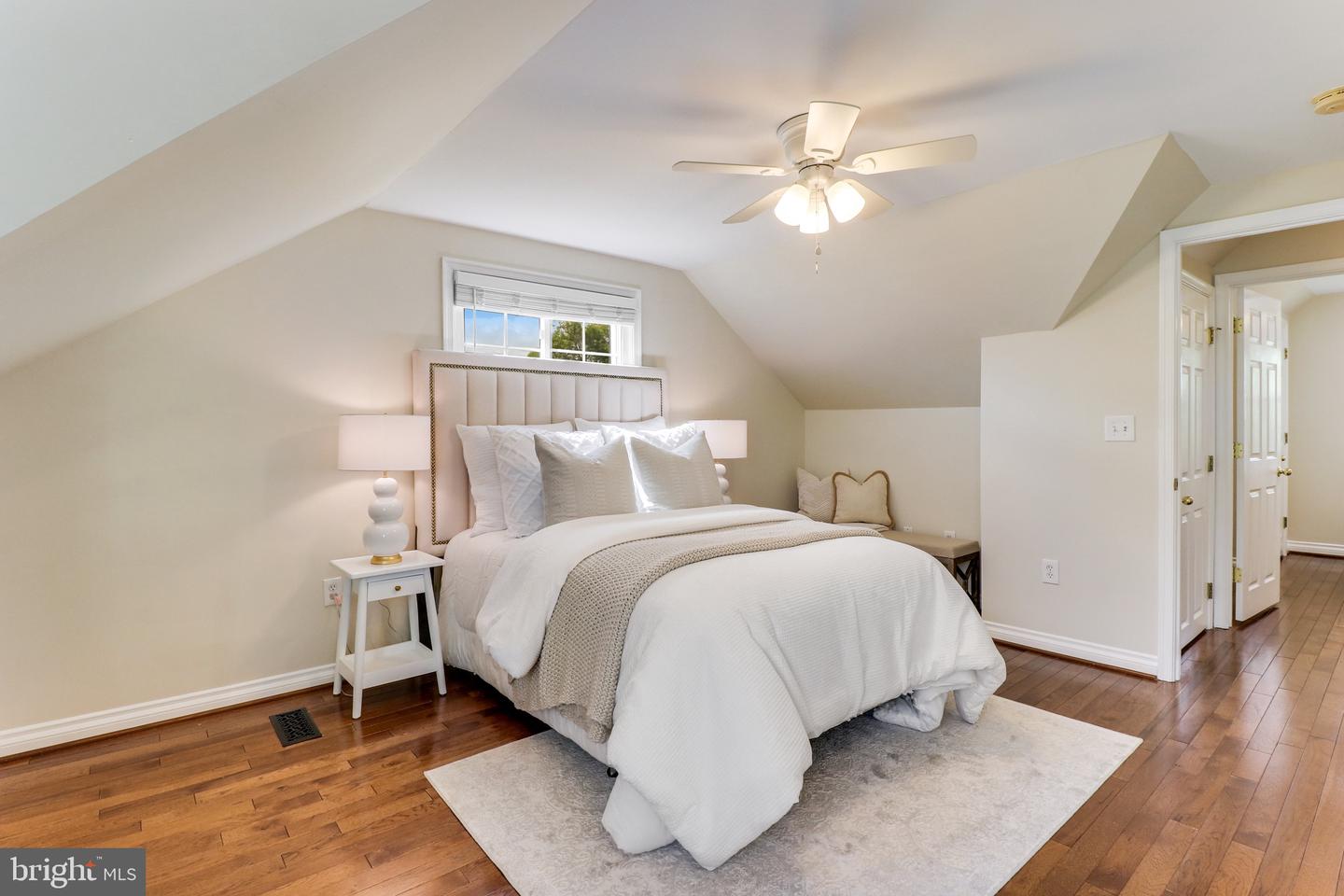 Staged bedroom with a large bed, sloped ceiling, hardwood floors, and ceiling fan.