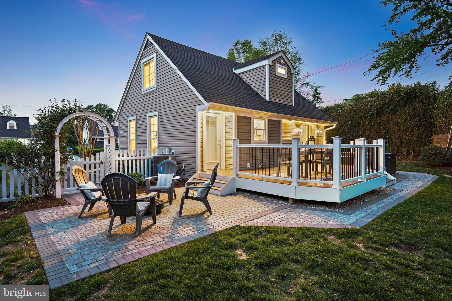 Gray-sided home with an illuminated raised deck and paved patio furnished with outdoor seating.