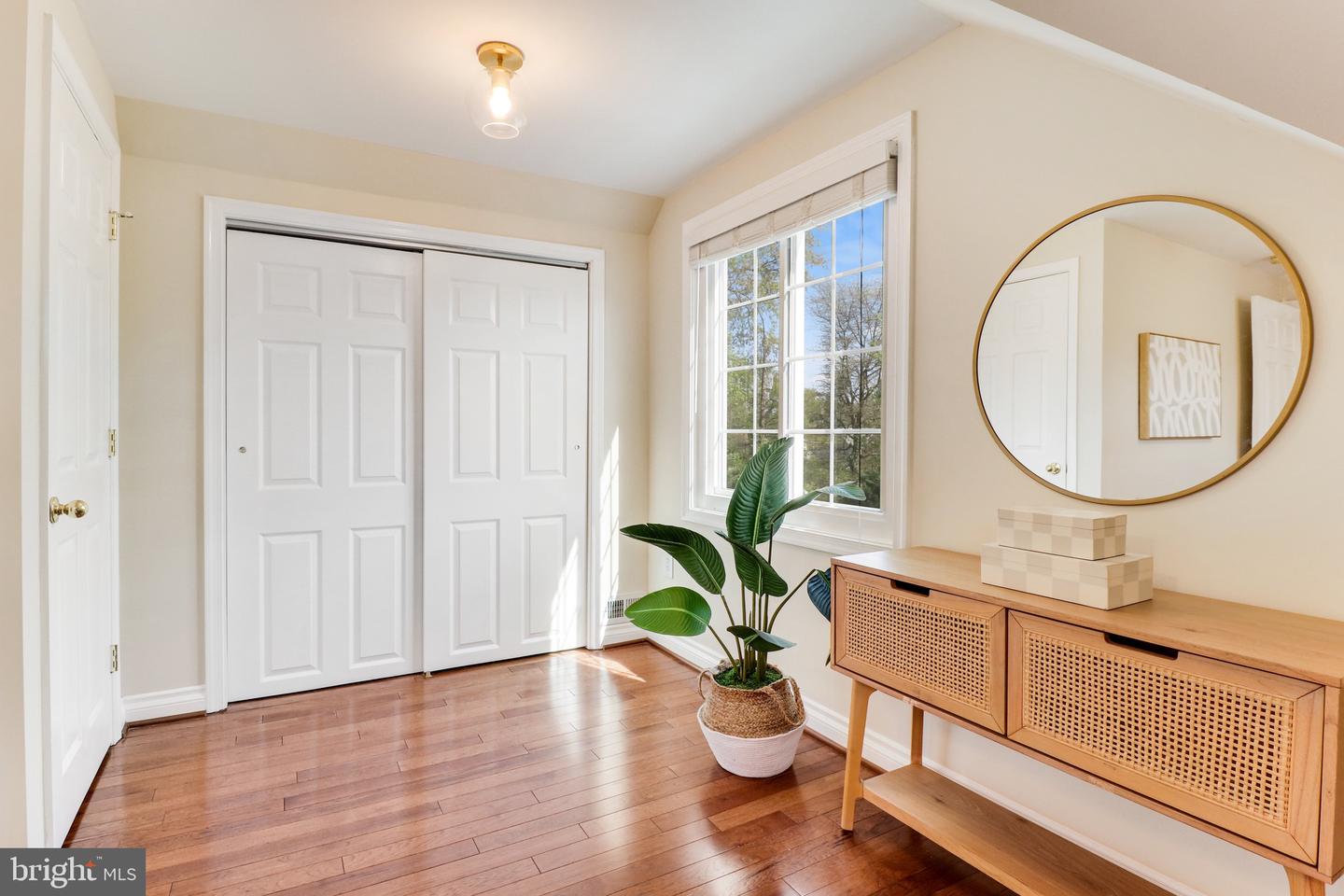 Bright bedroom with hardwood floors, sliding closet doors, and a sunlit window.