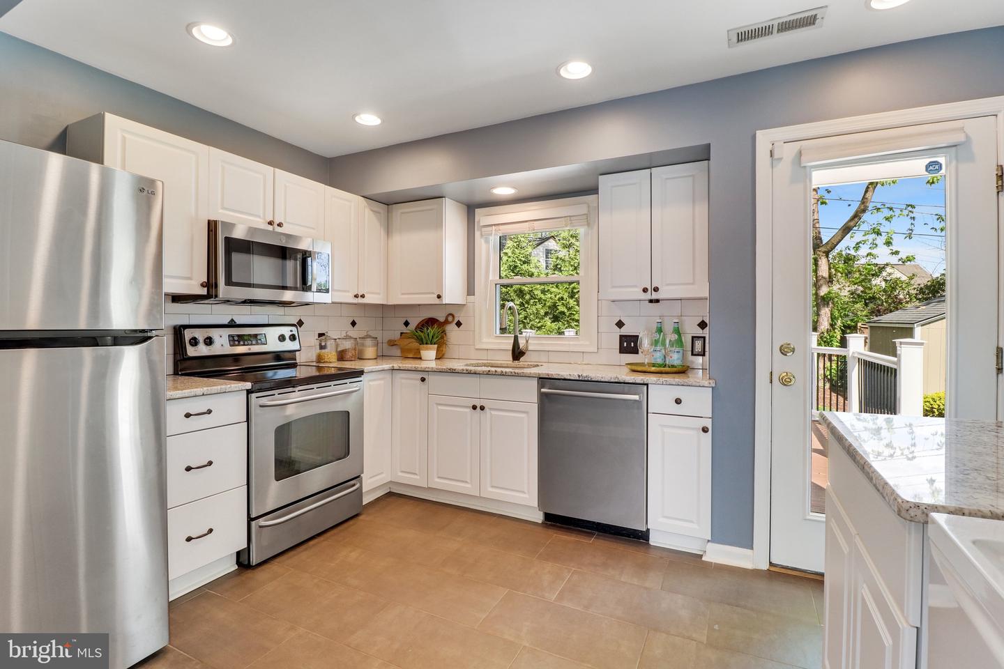 Kitchen with white cabinets, stainless-steel appliances, and a glass door opening onto a deck.