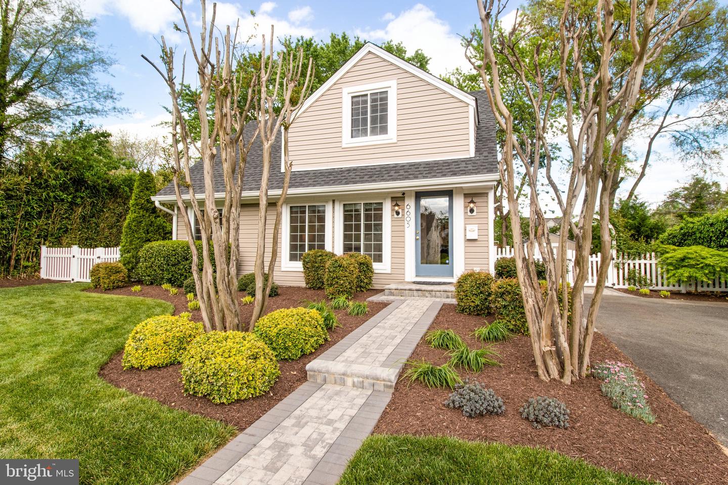 Beige two-story house with a blue front door, landscaped garden beds, and a paved walkway.