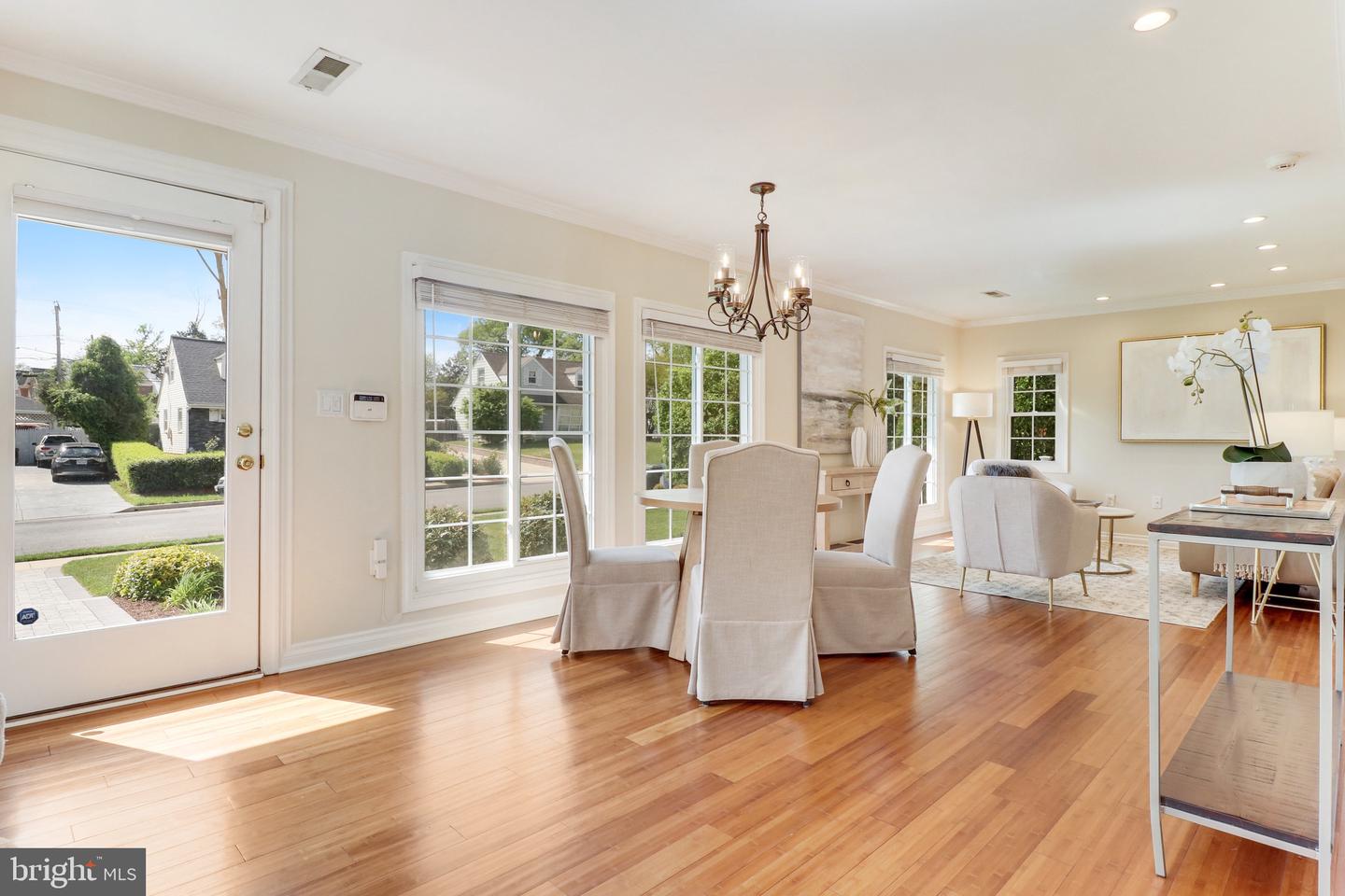 Dining and living area with hardwood floors, large windows, and neutral furnishings.