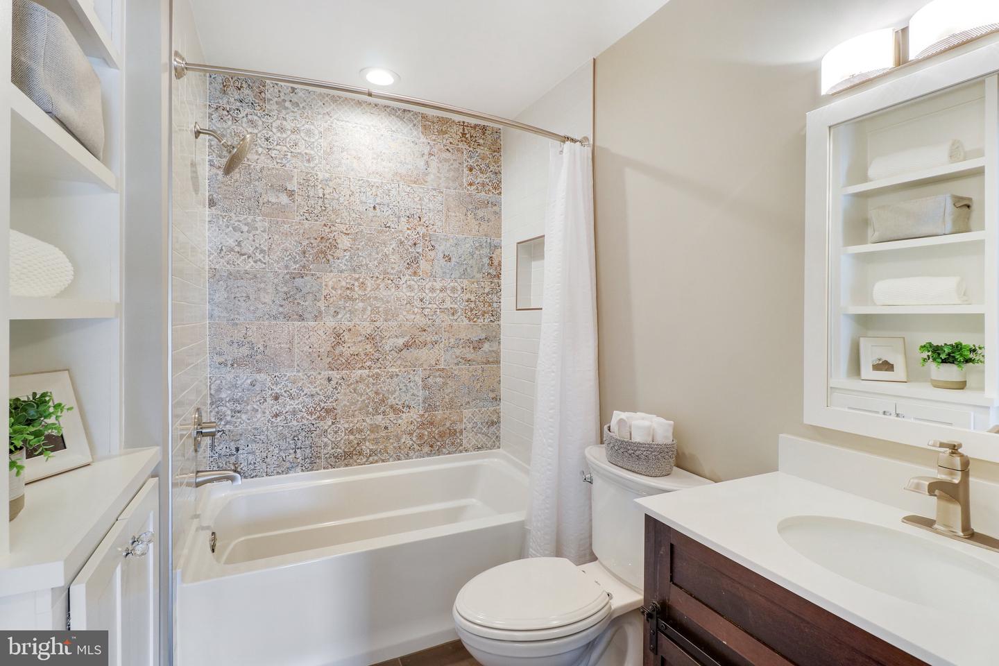 Bathroom with a patterned tile tub surround, white bathtub, and dark wood vanity.