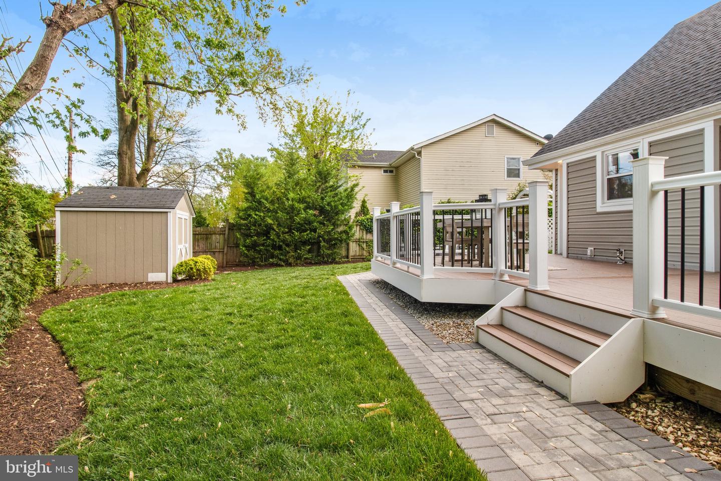Backyard with a raised deck, paved walkway, green lawn, and garden shed.