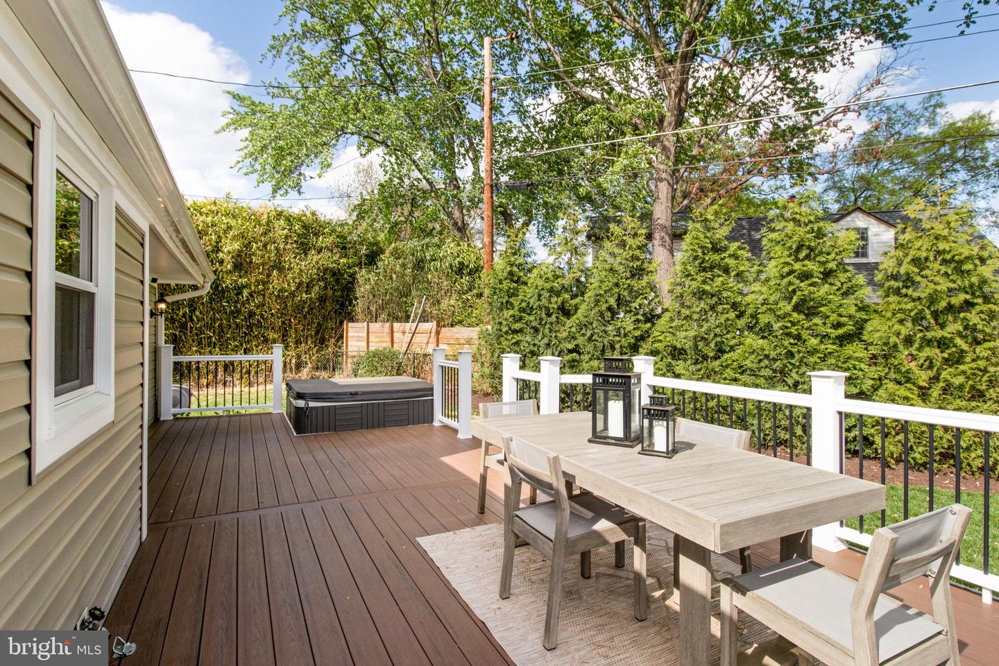 Outdoor deck with dining furniture, a hot tub, and tall privacy hedges.