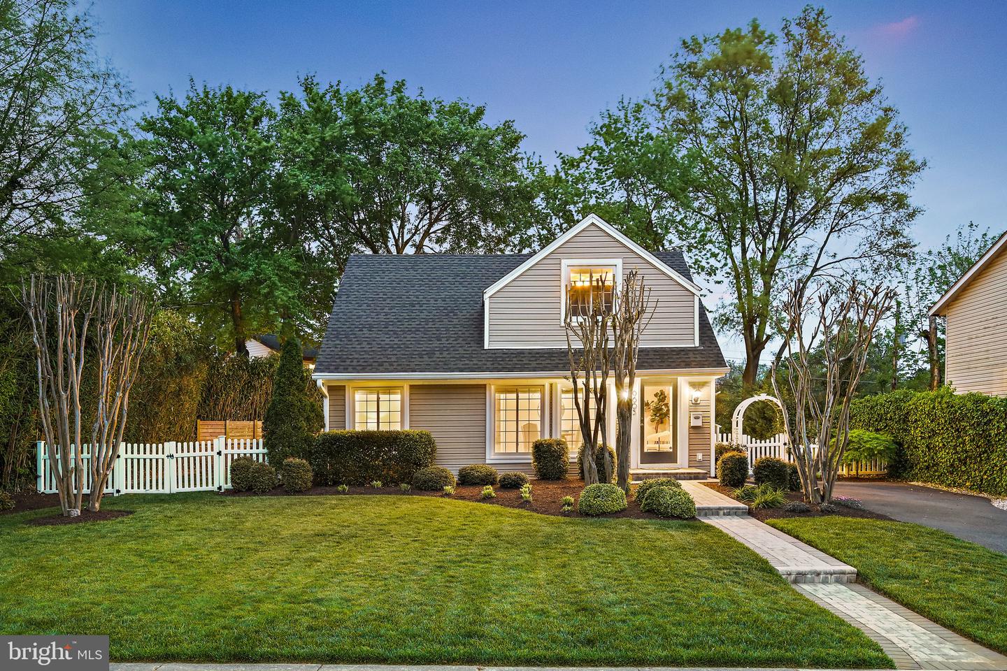 Gray two-story house with a white picket fence and stone walkway, photographed at dusk.