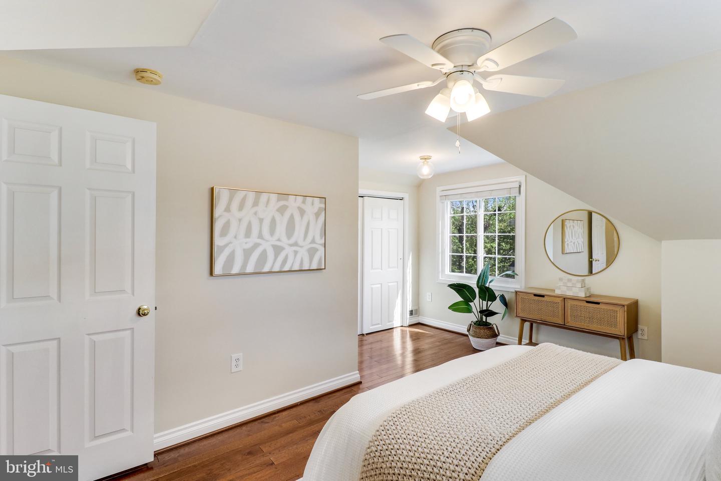 Bedroom with a sloped ceiling, ceiling fan, hardwood floors, and a window overlooking greenery.