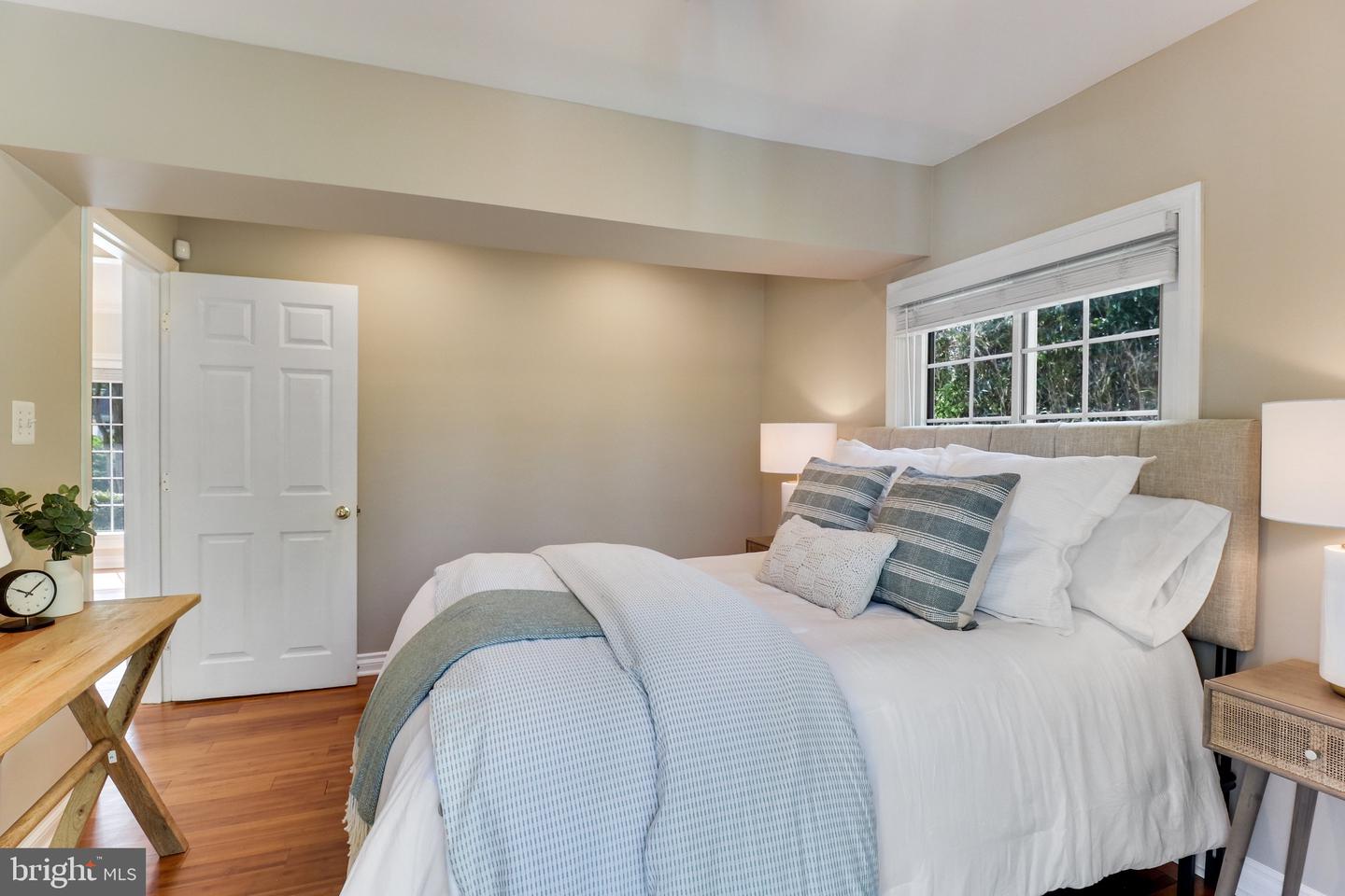 Staged bedroom with a white bed, blue-gray throw, upholstered headboard, and wide window.
