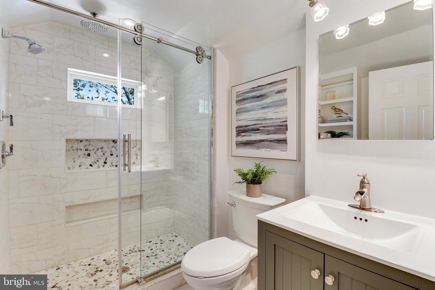 Bathroom with a glass walk-in shower, marble-look tile, pebble accents, and dark vanity.