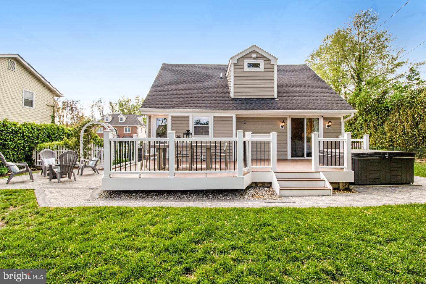 Rear of a gray house with a raised deck, patio seating, and a covered hot tub.