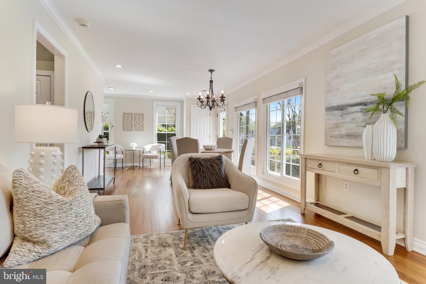 Staged living and dining room with cream seating, a chandelier, and large sunlit windows.