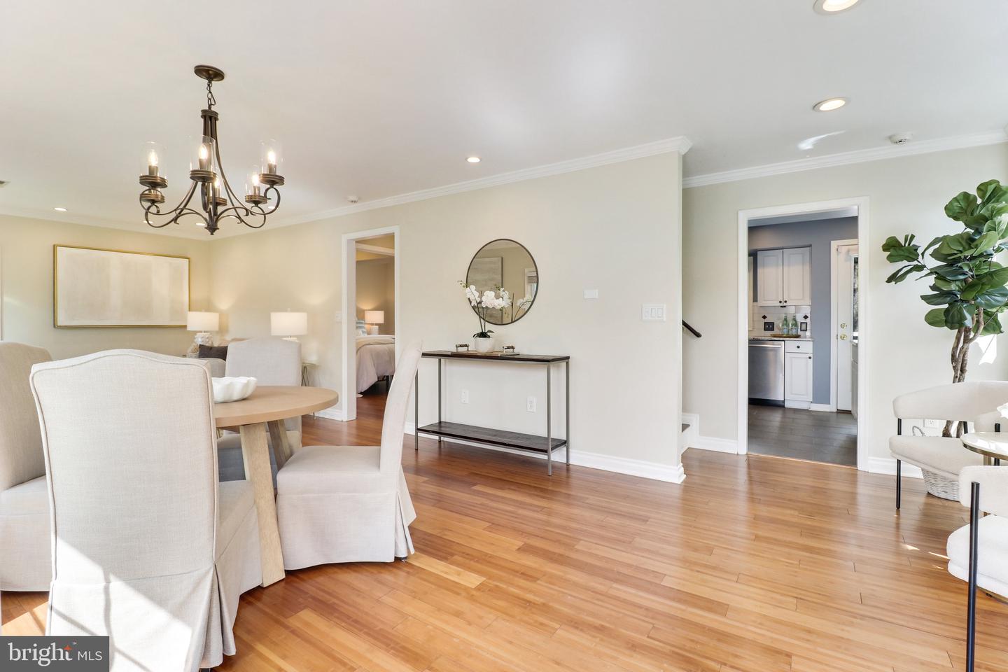 Dining area with hardwood floors, upholstered chairs, chandelier, and open views into the kitchen and bedroom.
