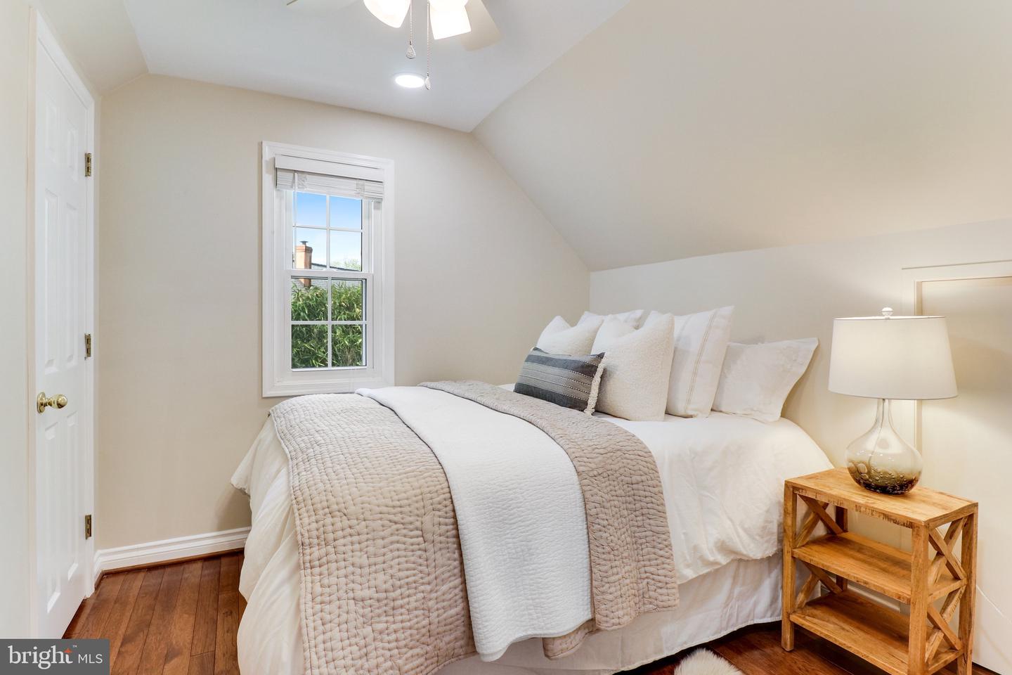 Staged bedroom with a large bed beneath a sloped ceiling and a window overlooking greenery.