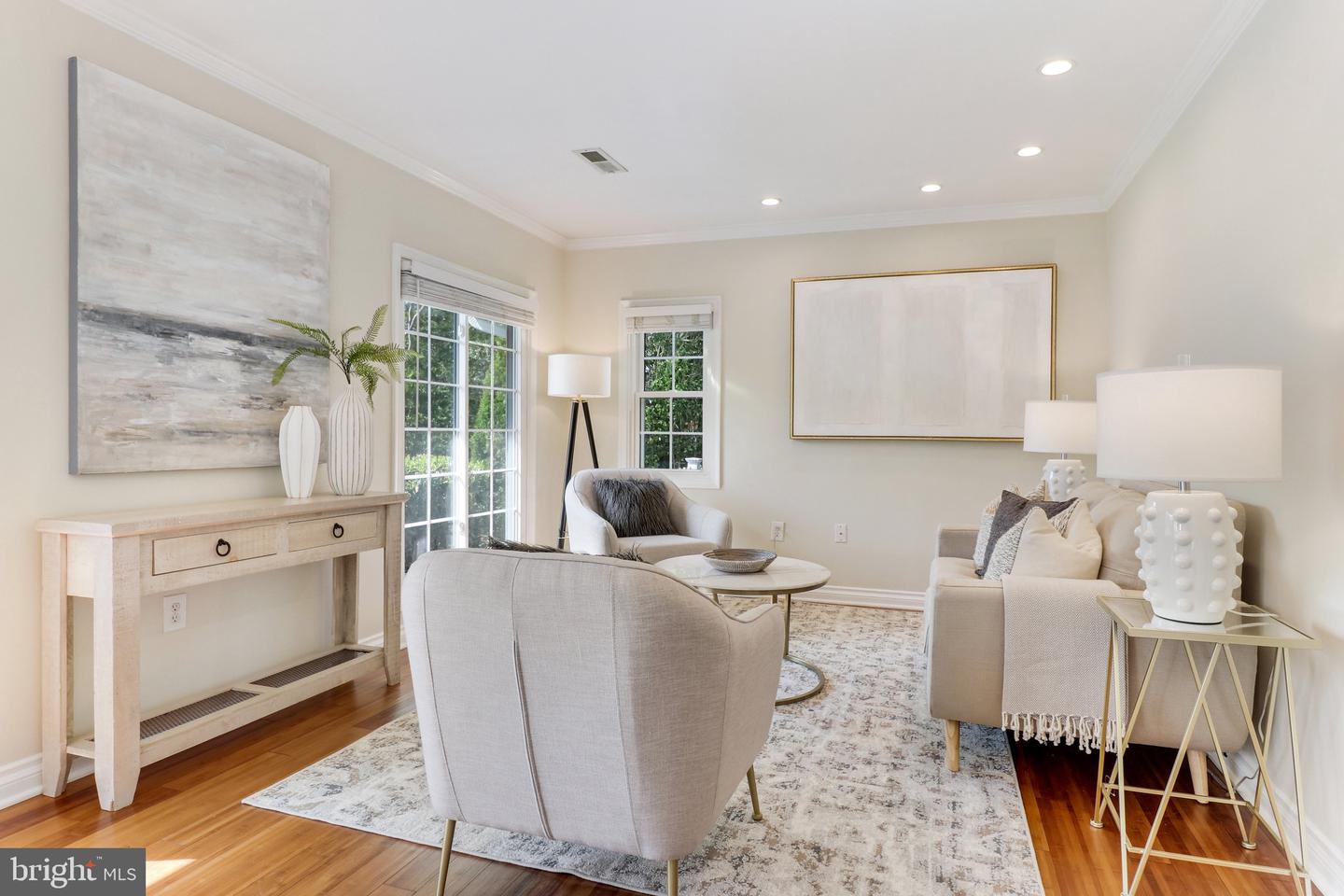 Staged living room with neutral seating, large windows, and hardwood floors.
