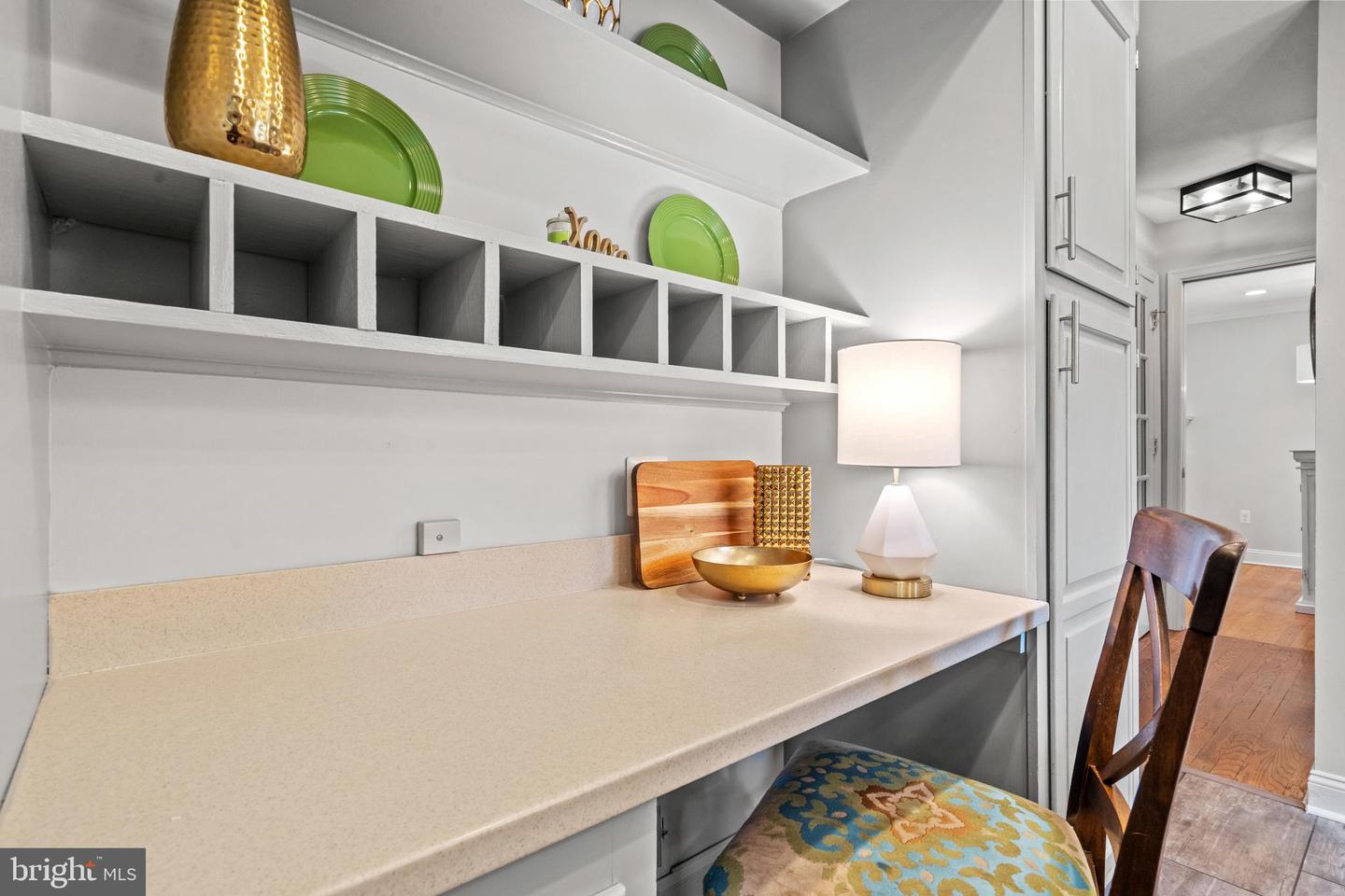 Built-in desk nook with white cubbies, a light countertop, and a wooden chair with a colorful seat.