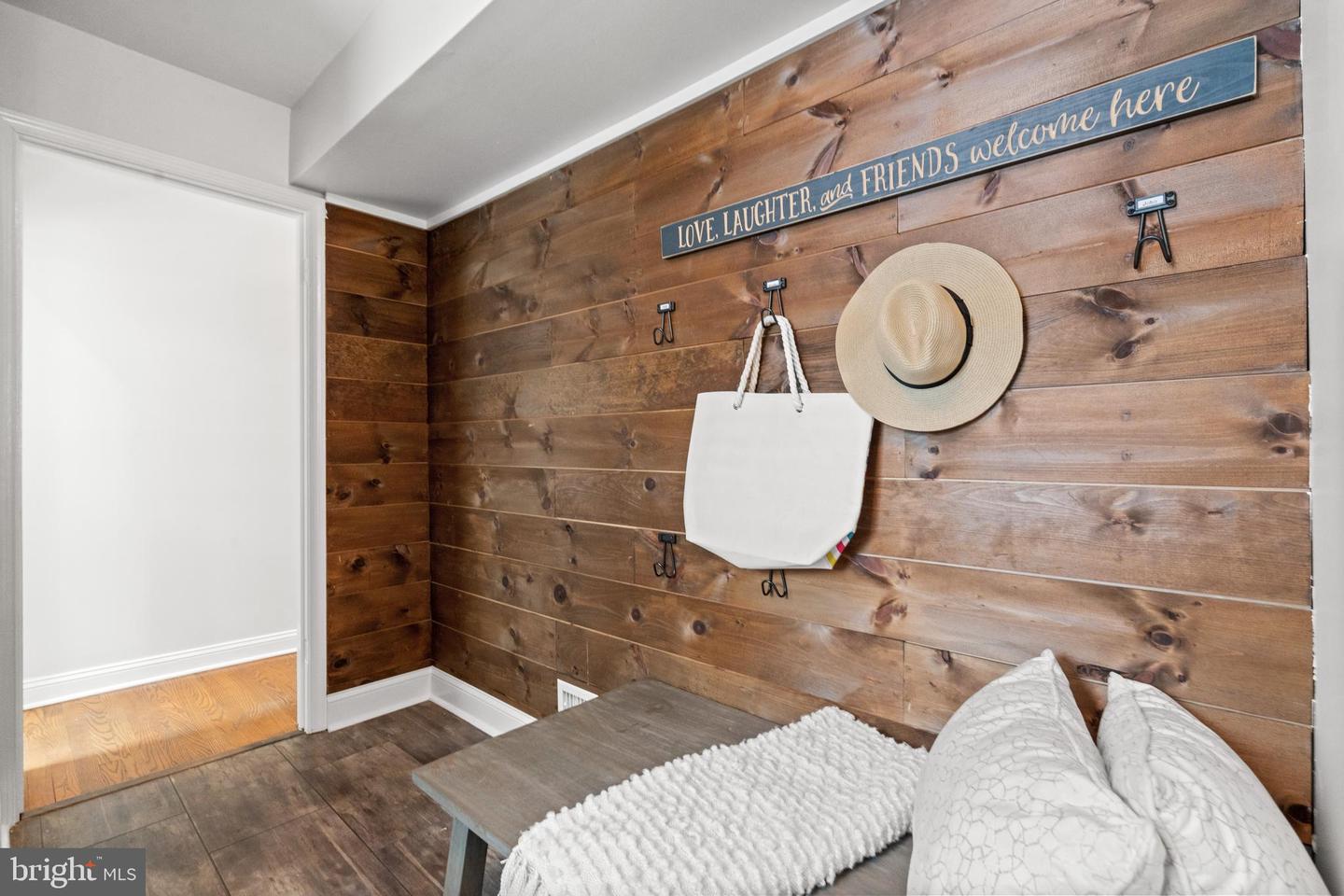 Entryway nook with a rustic wood-plank wall, hooks, straw hat, tote bag, and cushioned bench.