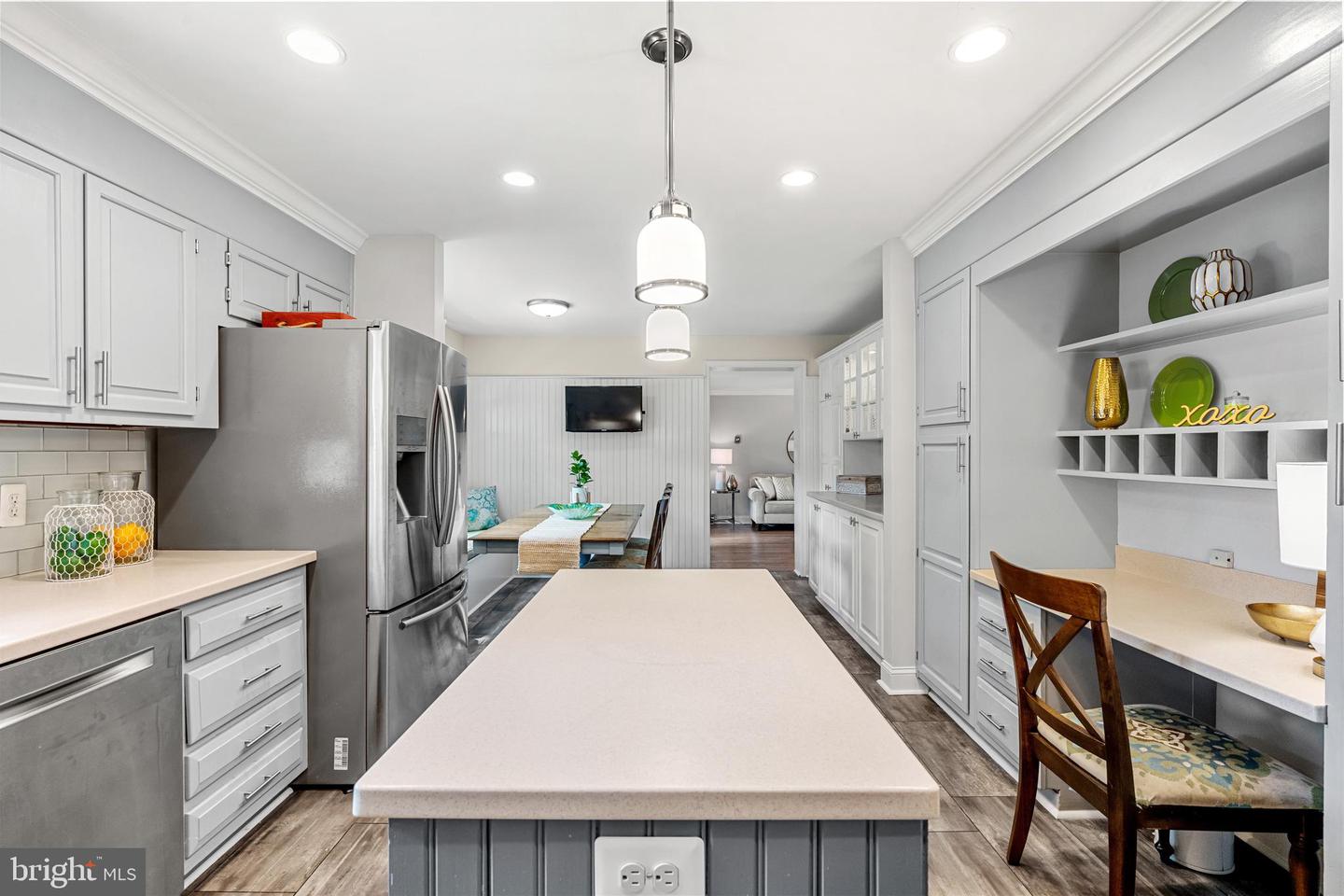 Kitchen with a large island, gray cabinetry, stainless steel refrigerator, and built-in desk nook.