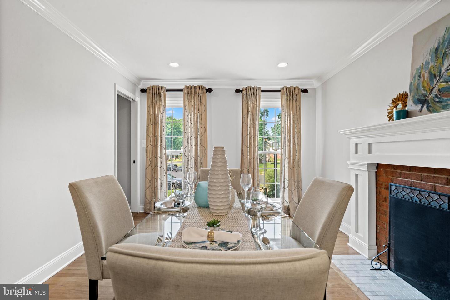 Dining room with a set glass-top table, curtained windows, and a brick fireplace.