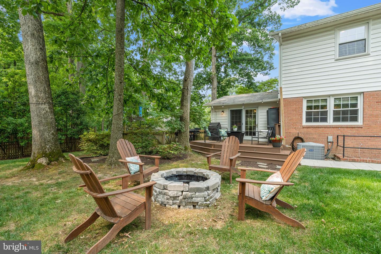 House backyard with a raised deck and Adirondack chairs around a stone fire pit.