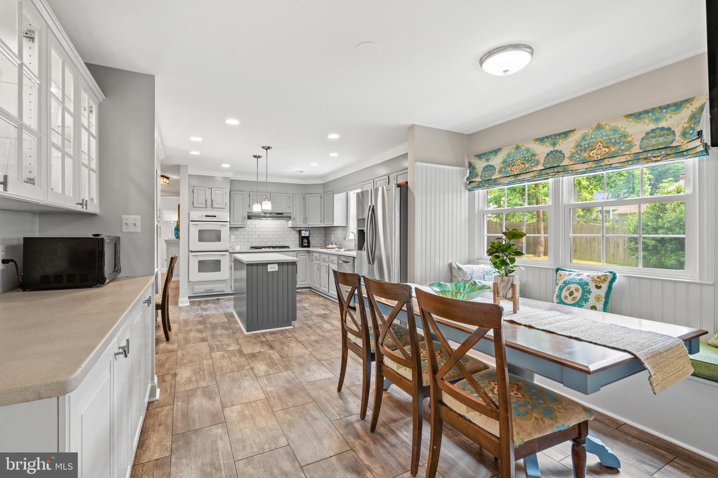 Kitchen and dining area with a gray island, stainless steel appliances, and a window bench with colorful cushions.