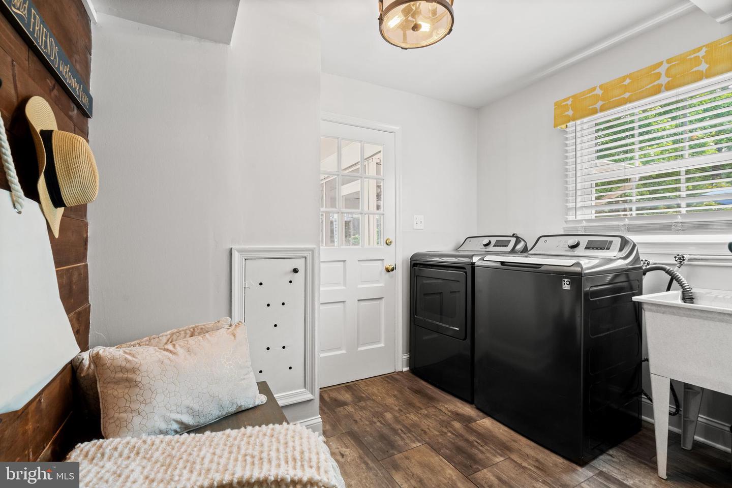 Laundry room with black washer and dryer, utility sink, and cushioned bench.