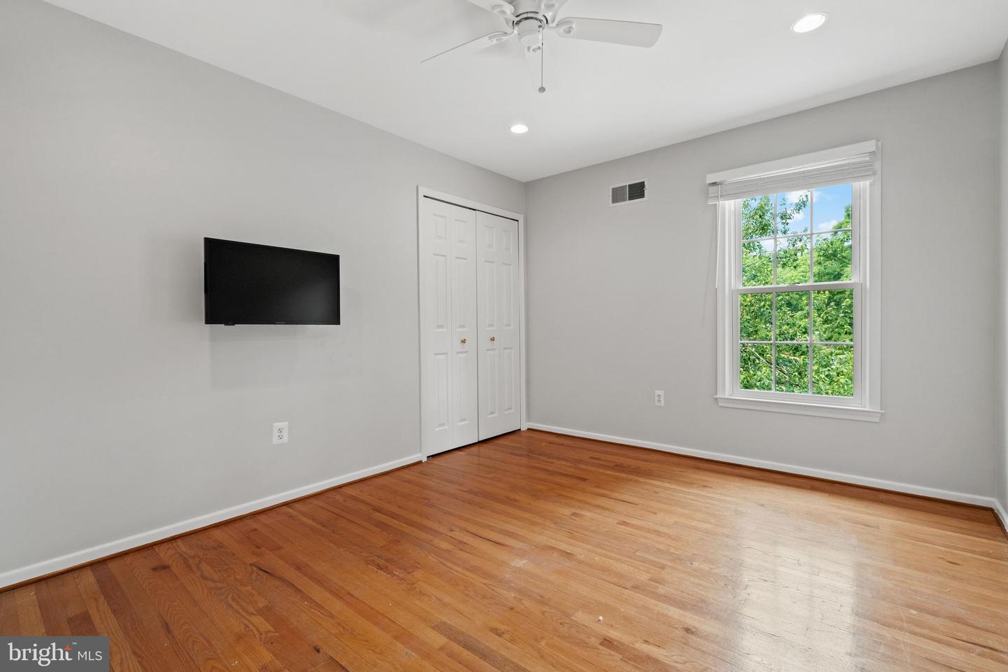 Unfurnished bedroom with hardwood floors, a ceiling fan, double closets, and a large window.