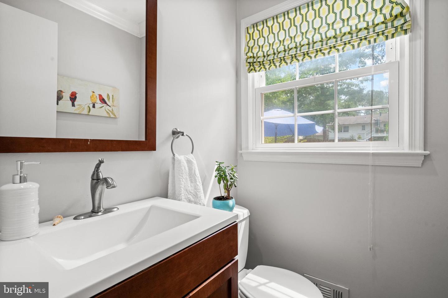 Bathroom with dark wood vanity, white sink, and a window topped by a patterned shade.