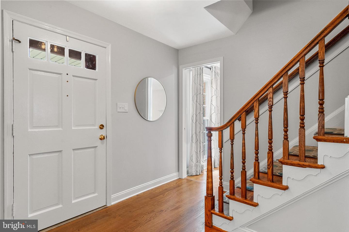 Entry foyer with a white front door, hardwood floor, and polished wood staircase.